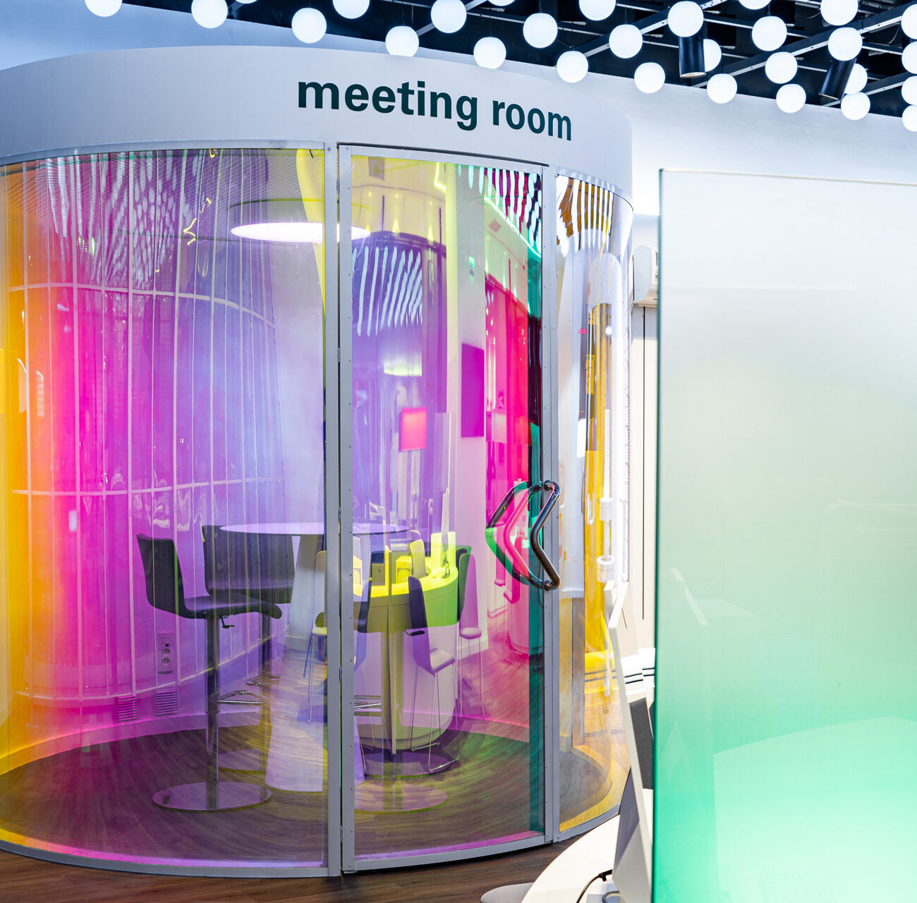 Enel Flagship Store retail project by STIRIXIS Group showing meeting room with colourful illuminated pods and translucent glass enclosure