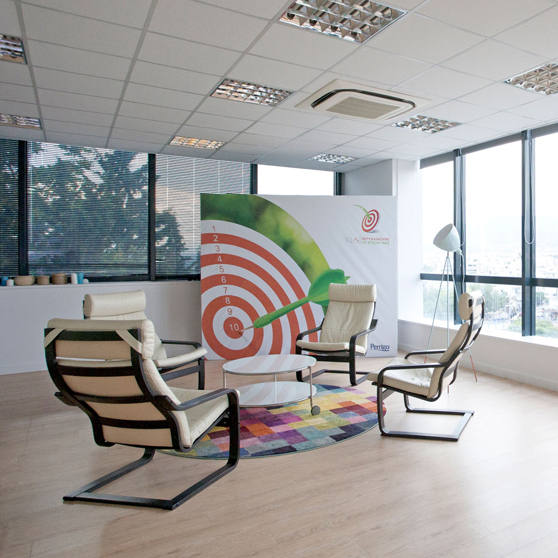 Perrigo Hellas workplace project by STIRIXIS Group showing lounge area with target graphic wall art and relaxed individual seating
