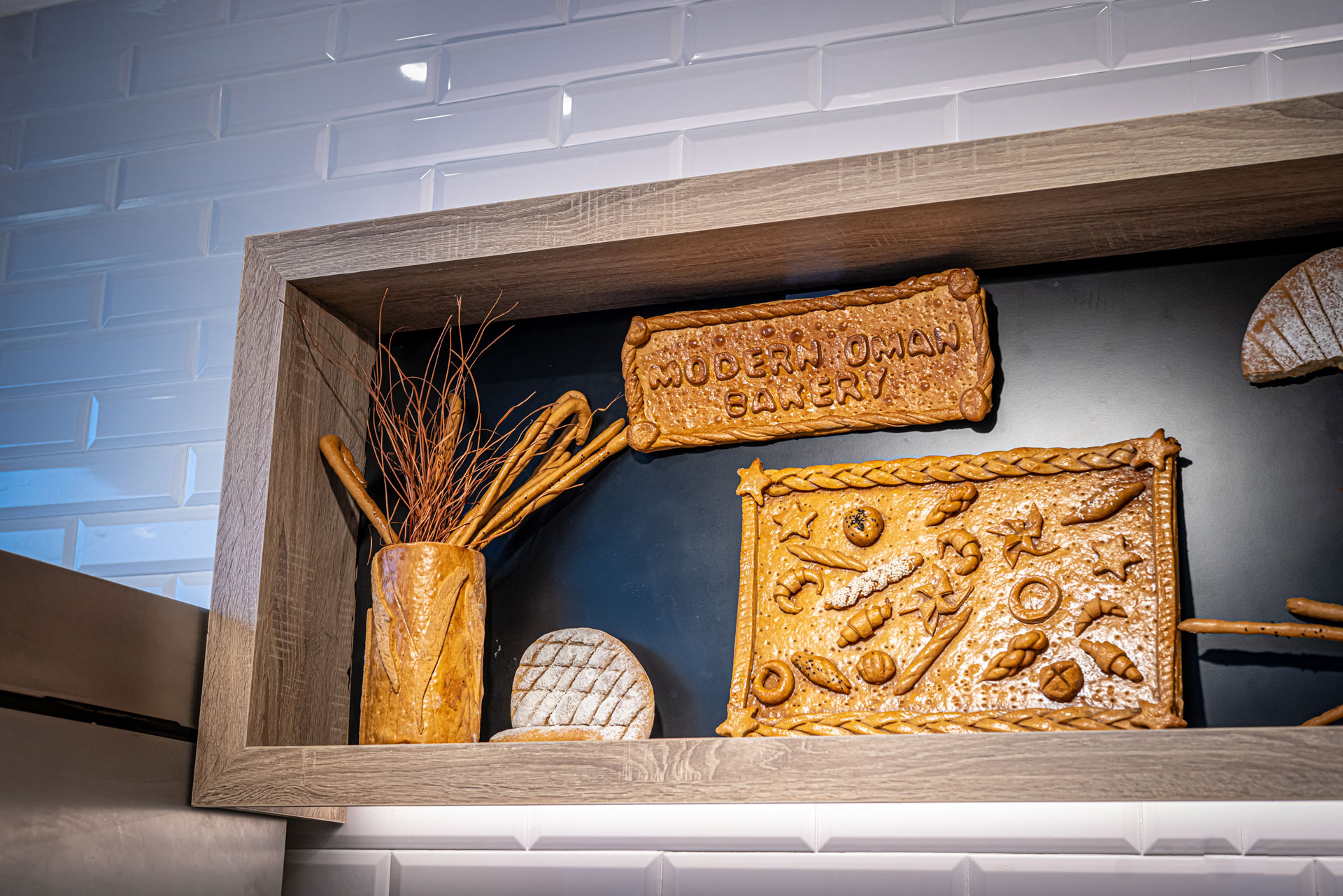 Modern Oman Bakery retail project by STIRIXIS Group showing wall display niche with handcrafted bread art pieces and Modern Oman Bakery signage