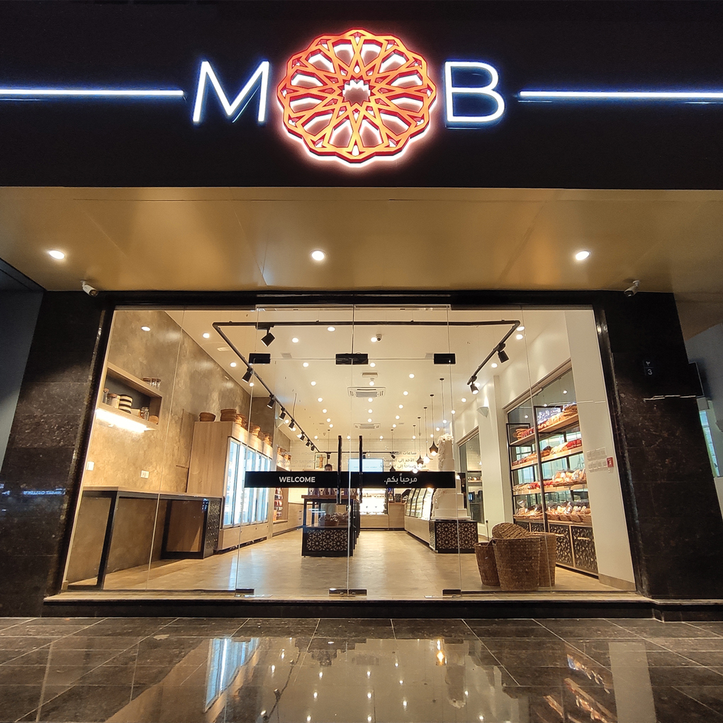 Modern Oman Bakery retail project by STIRIXIS Group showing exterior store facade at night with illuminated MOB logo and welcome entrance