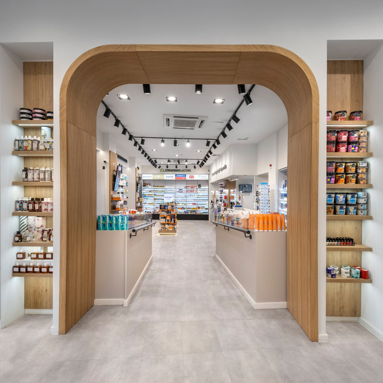 Panopoulos Pharmacy retail project by STIRIXIS Group showing interior arched entrance with warm wood finishes and product display shelving