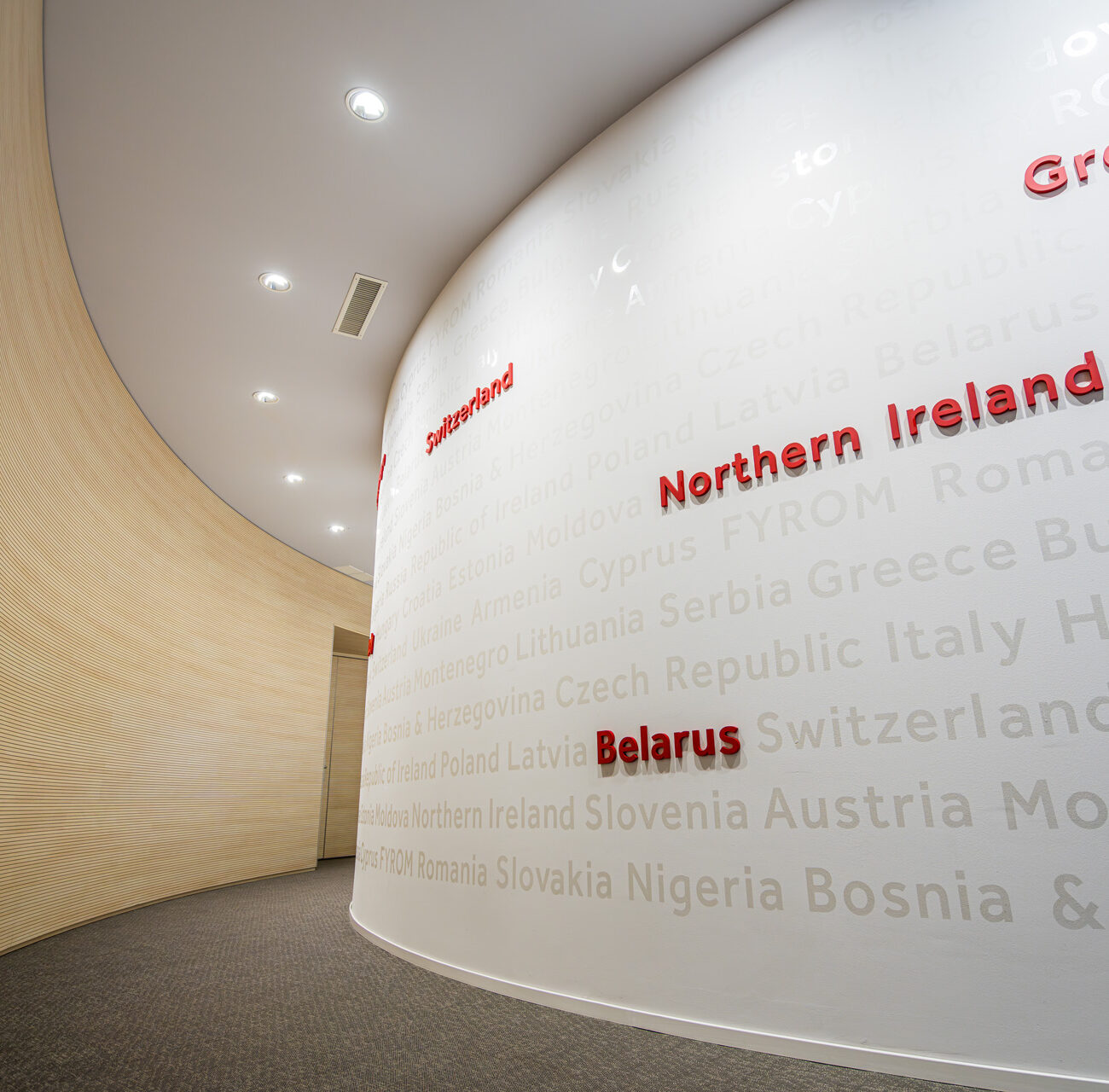 Coca-Cola HBC headquarters workplace project by STIRIXIS Group showing curved brand wall with country names representing the Coca-Cola HBC territory network