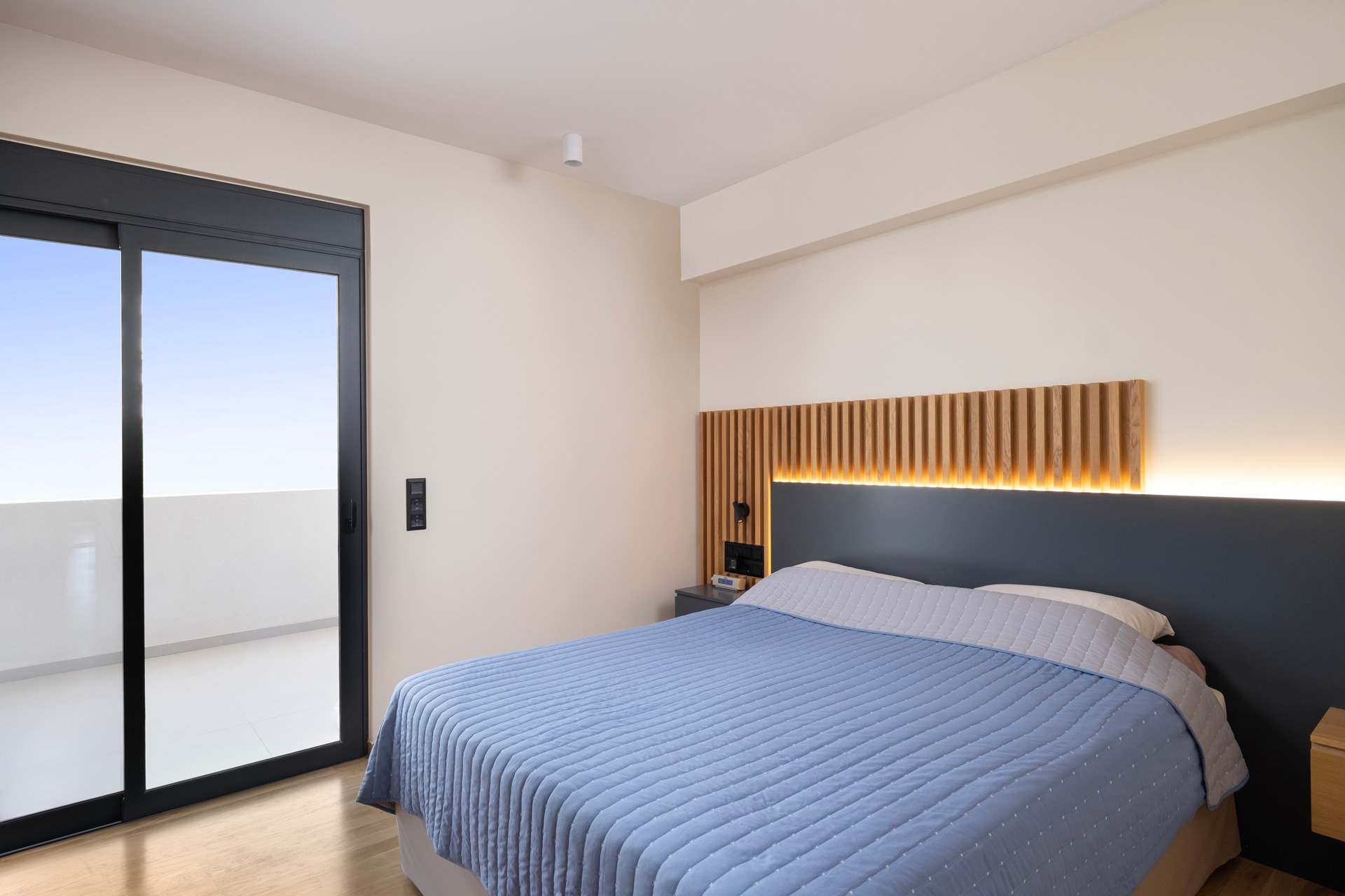 Contemporary Apartment by STIRIXIS Group showing bedroom with slatted wooden headboard, ambient lighting and balcony access