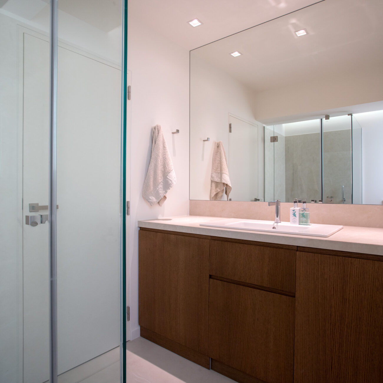 Pure Elegance residential project by STIRIXIS Group showing bathroom with wood vanity unit, large mirror and soft ambient lighting