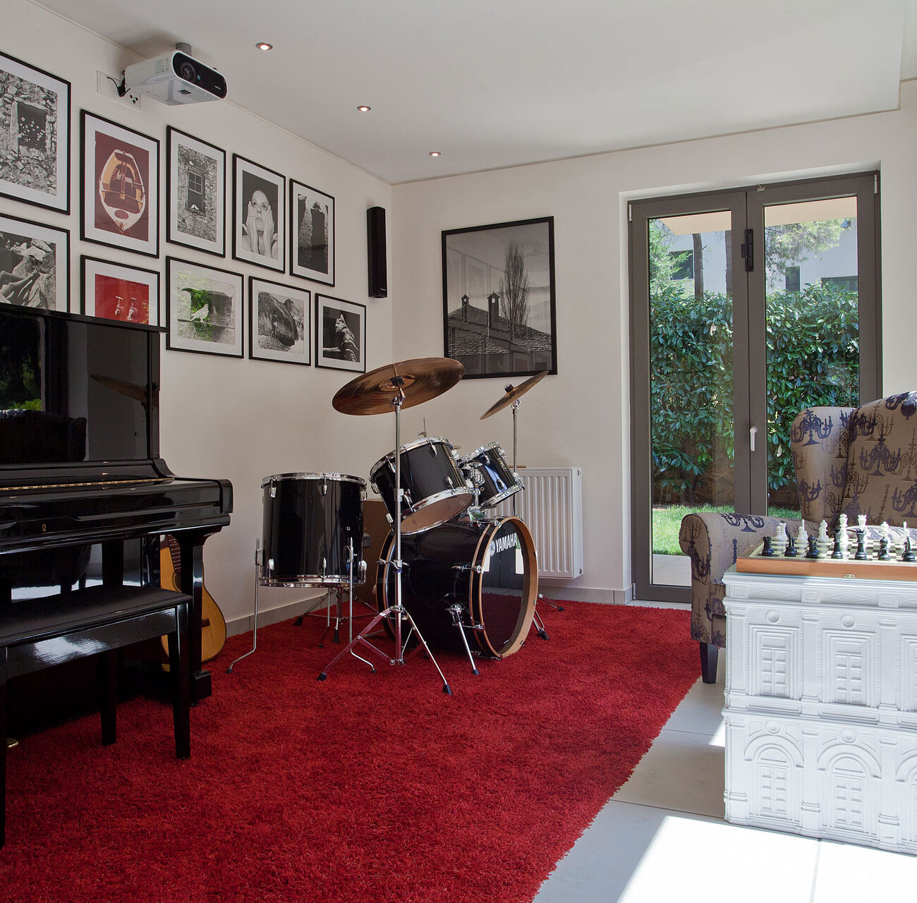 The Open House residential project by STIRIXIS Group showing music room with grand piano, red rug and framed gallery wall
