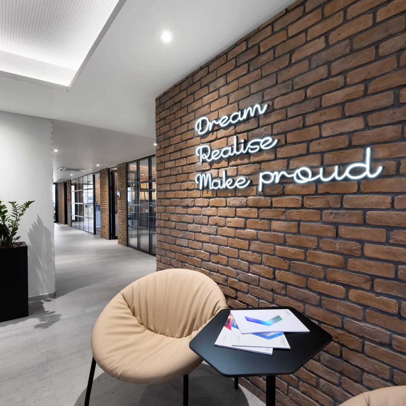 STIRIXIS Group Athens workplace project showing lounge area with exposed brick wall, motivational quote lettering and relaxed seating