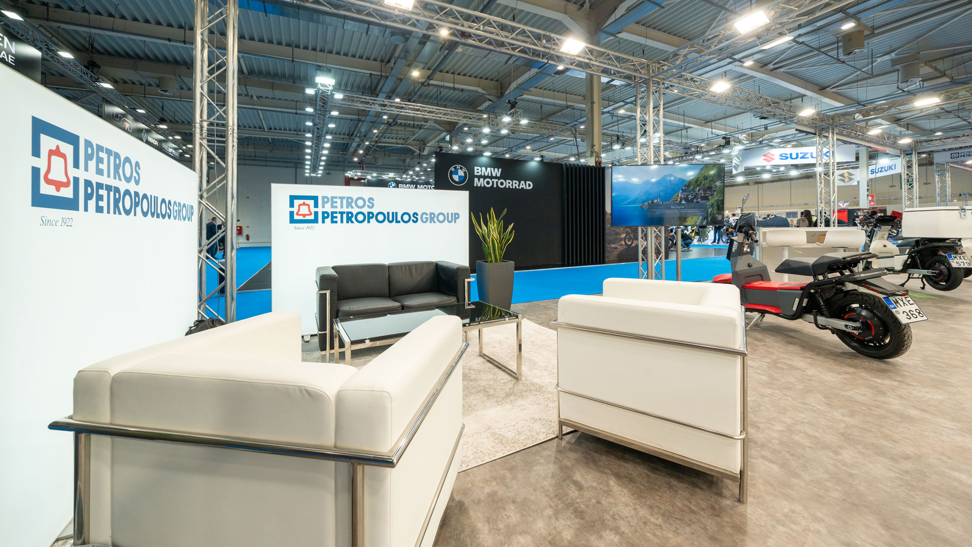 Petros Petropoulos Moto Expo exhibition stand by STIRIXIS Group showing lounge area with branded Petros Petropoulos backdrop and electric motorcycle display