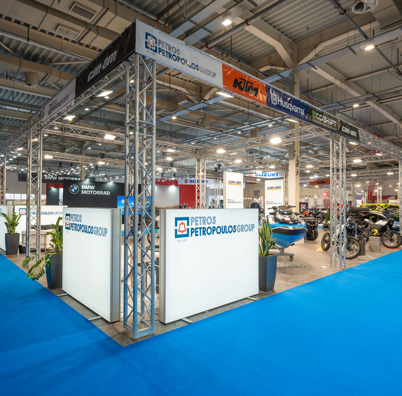 Petros Petropoulos Moto Expo exhibition stand by STIRIXIS Group showing full stand overview with blue carpet, branded signage and motorcycle lineup